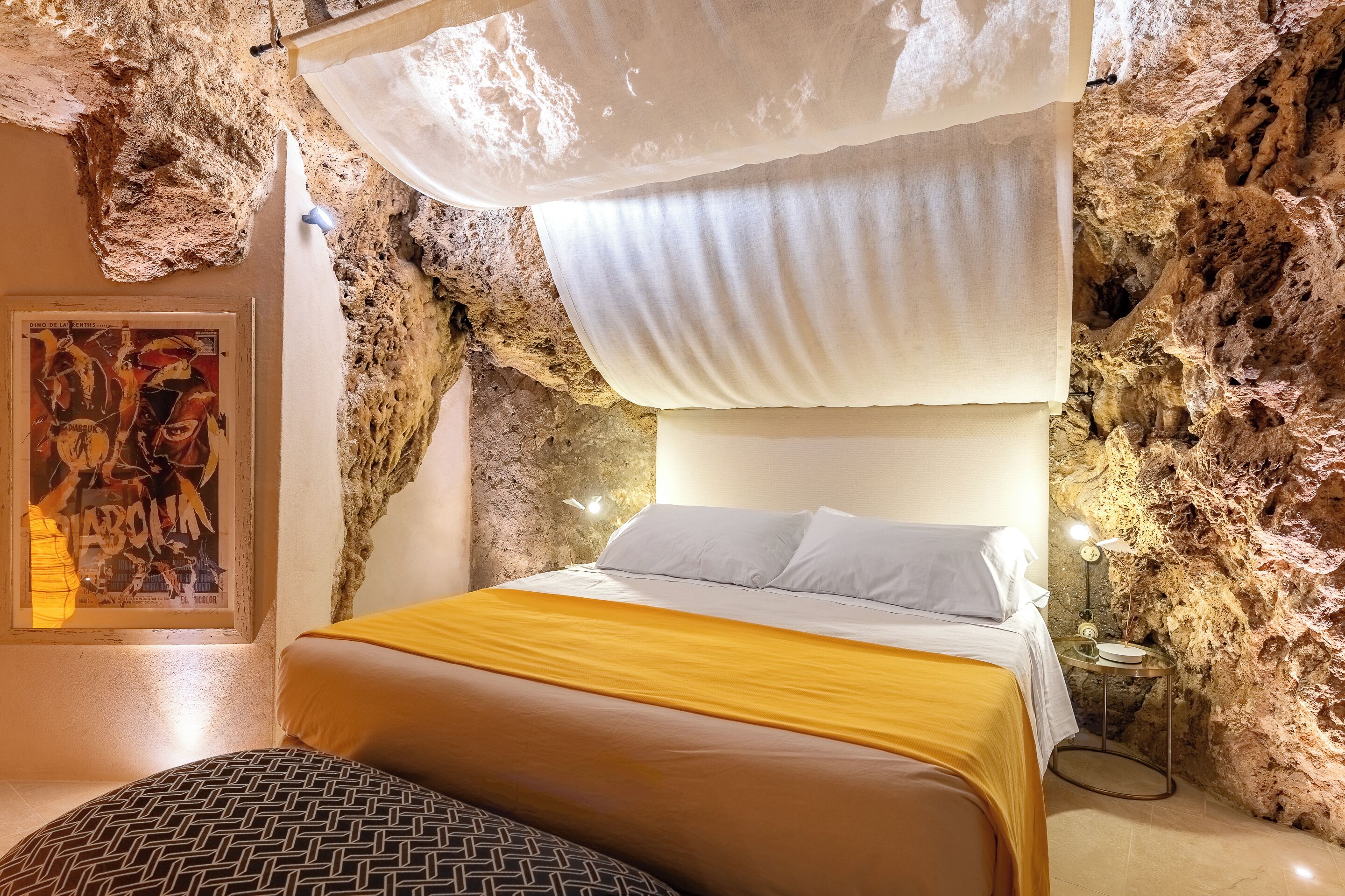 Een slaapkamer met een bed, nachtkastje en een wand met een structuur die doet denken aan een grot.
