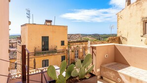A balcony with a cactus plant, a view of neighboring buildings, and a clear sky.