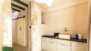 A narrow hallway with a green chair, a white door, and a kitchen area with a countertop, sink, and cabinets.