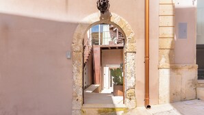 An arched doorway leading to a stairway with a potted plant and a metal pipe on the right.