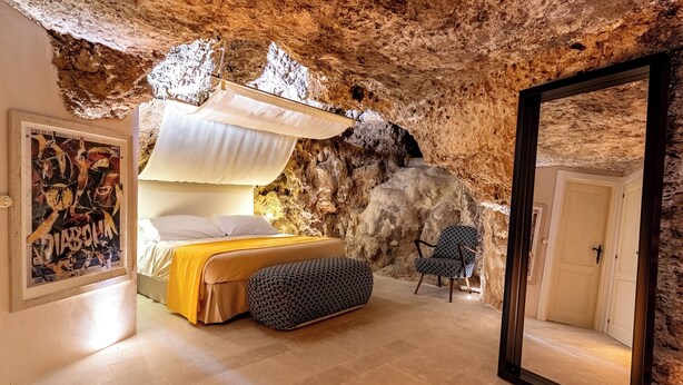 A bedroom with a bed, a chair, a mirror, and a wall with a rock-like texture.