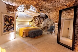 Una camera da letto con un letto, una sedia, uno specchio e una parete dalla texture simile a roccia.