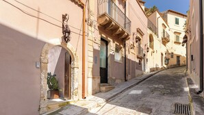 A narrow cobblestone street flanked by buildings with arched doorways and balconies.