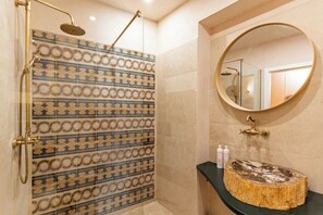 Un bagno con parete della doccia decorata, uno specchio rotondo e un lavabo in legno.