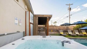 Un jacuzzi con piscina al fondo, una terraza de madera y sillas de descanso.