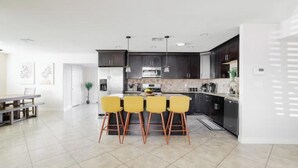 Una cocina moderna con armarios oscuros, una isla central con sillas amarillas y un comedor con mesa y sillas.