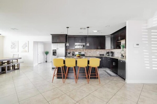 Une cuisine moderne avec des meubles de couleur sombre, un îlot central doté de chaises jaunes et un coin repas avec une table et des chaises.