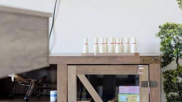 Un mueble de madera con puerta de cristal, que contiene una caja del juego Monopoly y un pequeño globo terráqueo.