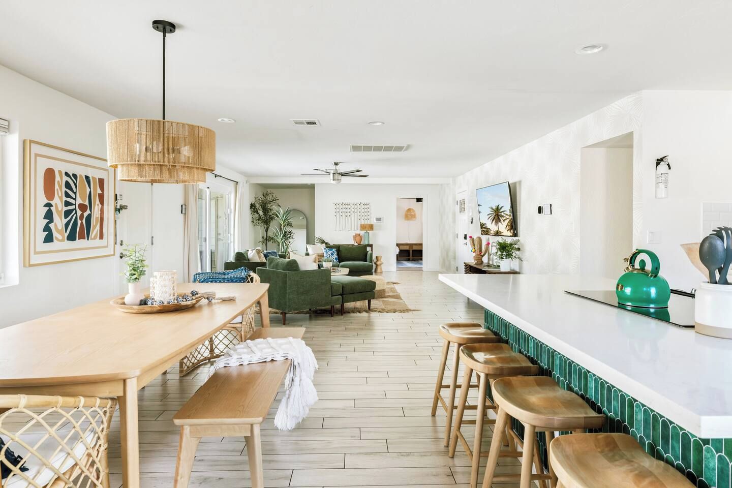 A modern kitchen with a dining area, wooden flooring, and a green kettle on the counter.