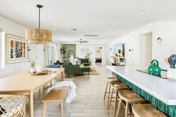 A modern kitchen with a dining area, wooden flooring, and a green kettle on the counter.