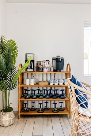 A room with a bamboo shelf holding mugs, a coffee maker, and a kettle.
