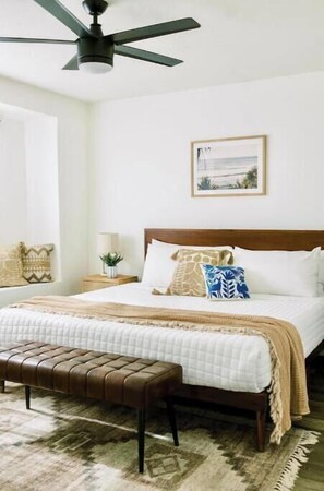 Una camera da letto con un letto, una panca, una ventola a soffitto, un comodino e un quadro incorniciato appeso al muro.