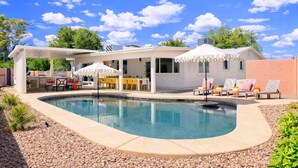 A swimming pool with a covered patio area, outdoor seating, and a clear blue sky.