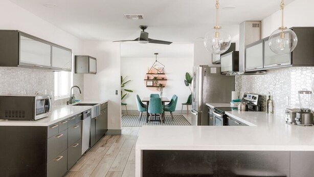 A modern kitchen with dark cabinetry, a central island, and a dining area with teal chairs.