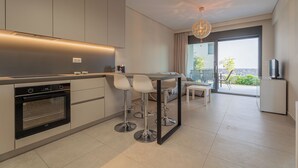 A modern kitchen with a built-in oven, a dining area with a bar stool, and a large window offering a view of the outdoors.