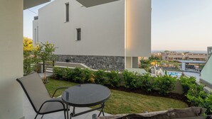 A modern outdoor patio with a round table and chairs, a stone wall, and a view of a swimming pool and buildings in the background.