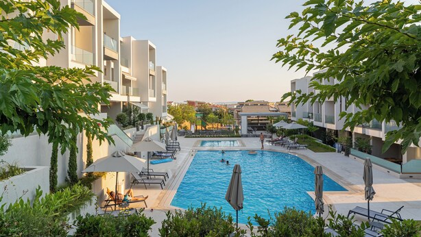 A swimming pool surrounded by lounge chairs and umbrellas, with a view of modern buildings in the background.