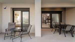 A modern apartment with a dining area, a kitchen, and a living space with a sofa and a glass door leading to a balcony.