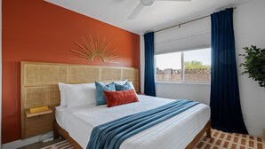 Een slaapkamer met een bed, nachtkastje, wanddecoratie, raam met gordijnen en een plafondventilator.