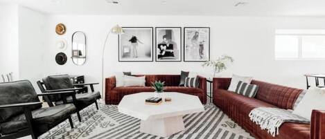 A modern living room with a red sofa, black chairs, a white coffee table, and patterned rugs.
