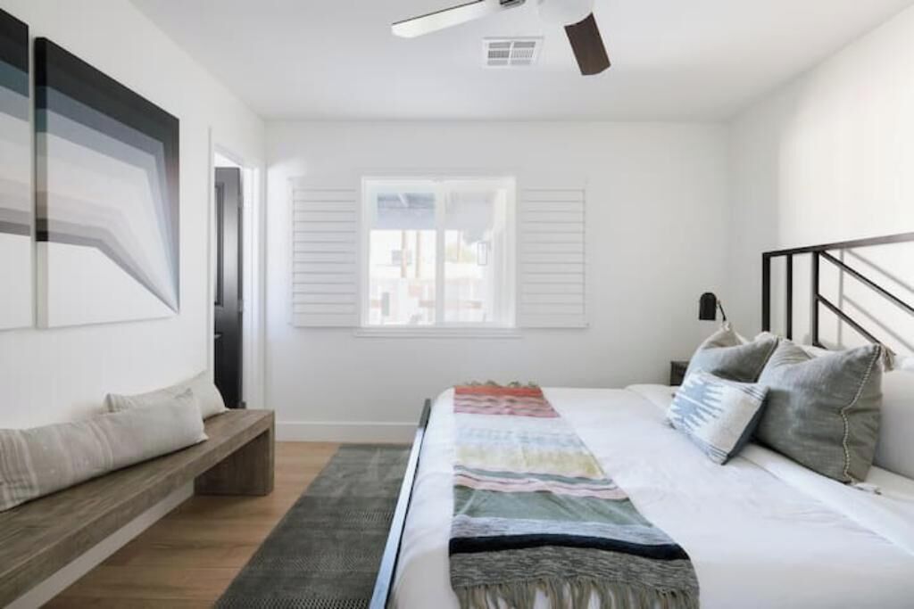 Una camera da letto moderna con un letto grande, una panca, una finestra con persiane e una ventola a soffitto.