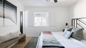 Una camera da letto moderna con un letto grande, una panca, una finestra con persiane e una ventola a soffitto.