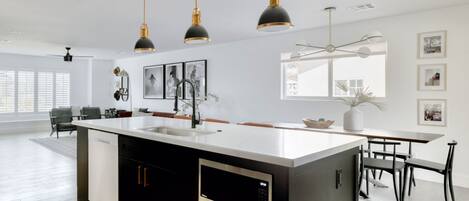 A modern kitchen with a central island, pendant lighting, and a dining area with a table and chairs.