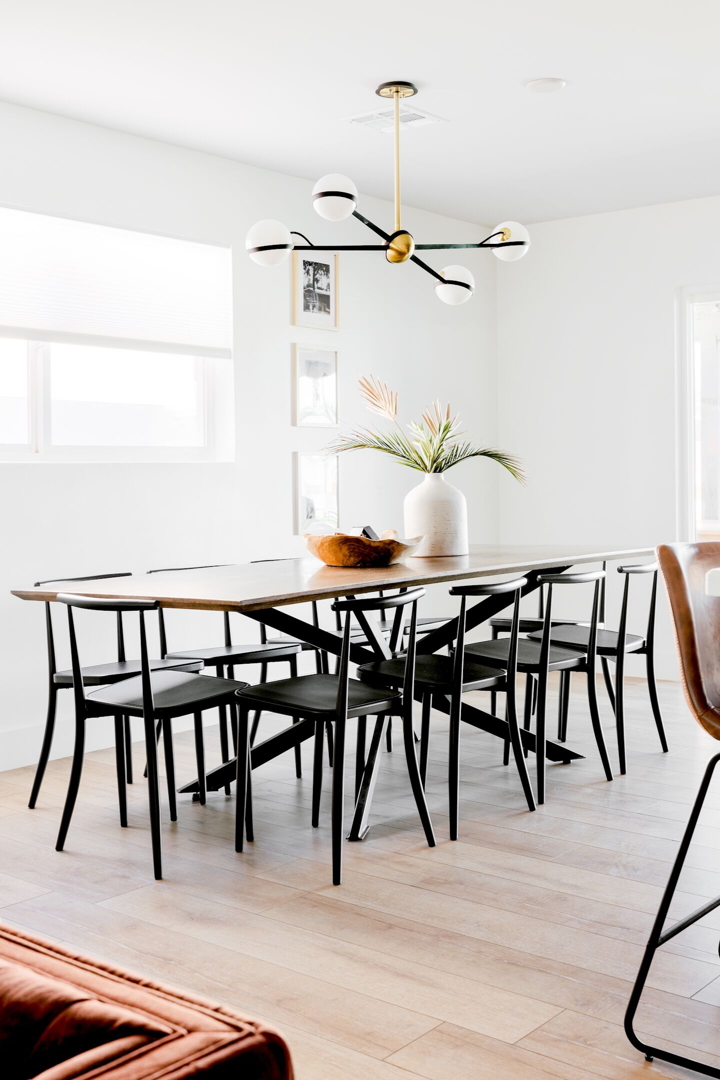 A modern dining area with a wooden table surrounded by black chairs, a white vase with plants, and a unique ceiling light fixture.