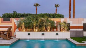A swimming pool with a tiled deck, surrounded by palm trees and a decorative wall with geometric patterns.