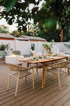 Un espacio de comedor al aire libre con una mesa de madera dispuesta para seis personas, rodeado de sillas de mimbre.