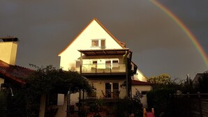 A two-story house with a balcony, surrounded by vegetation.