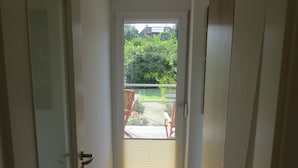 A narrow hallway leading to a door with a view of a garden and outdoor furniture.