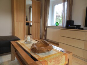 A room with a wooden table, a bowl, a glass, a radiator, a window with curtains, a television, and a sofa.