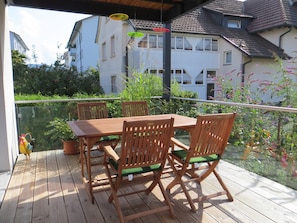 A wooden deck with a table and chairs, surrounded by greenery and buildings. - Holiday Apartment 2, 65 sqm, balcony, 1 bedroom, max. 4 people (Grenzach-Wyhlen)