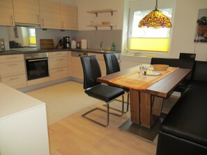 A modern kitchen with a dining area, wooden cabinets, a built-in oven, and a dining table with chairs. - Holiday Apartment 2, 65 sqm, balcony, 1 bedroom, max. 4 people (Grenzach-Wyhlen)