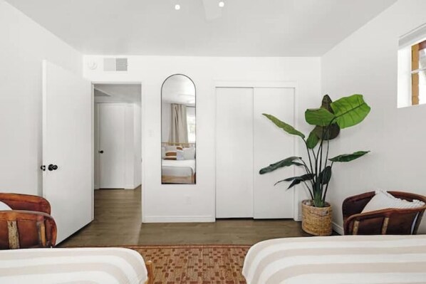 Une chambre d’hôtel avec un grand miroir, une plante en pot et deux chaises en bois.
