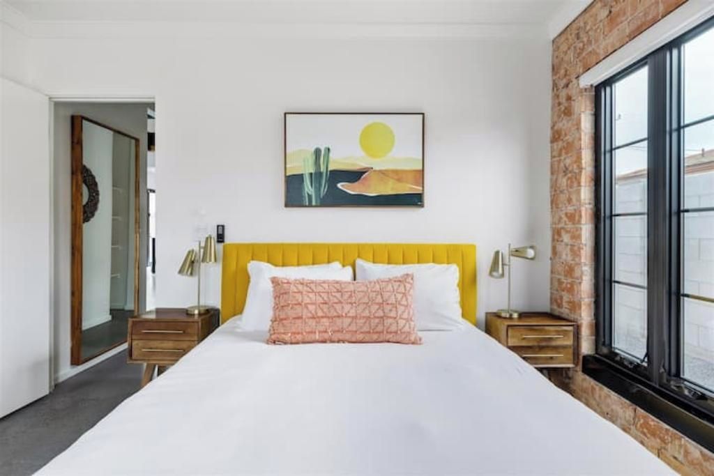 Ein Hotelzimmer mit einem großen Bett, einem gelben Kopfteil, einem Gemälde einer Wüstenlandschaft und einer Ziegelwand.
