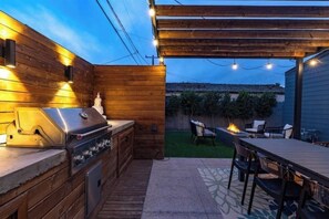 Un espace cuisine extérieur comprenant un barbecue, un four encastré et une table à manger avec des chaises.