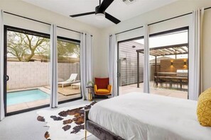 Une chambre avec un lit, un ventilateur de plafond et une vue sur une piscine et un espace de détente extérieur.