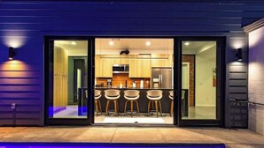 Cocina moderna con acceso por puerta de vidrio, piscina con iluminación azul y zona de bar con taburetes.