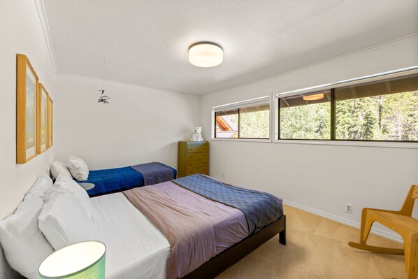 A bedroom with two beds, a dresser, a rocking chair, and a window with a view of trees.