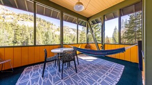 A room with a wooden ceiling, large windows, a hammock, a patterned rug, and a table with chairs. - Trapper Cabin in Alpine Meadows w/ hot tub (Alpine Meadows)