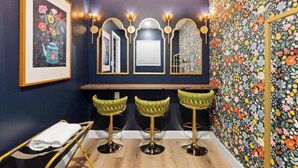 A bar area with three green bar stools, a wooden counter, and a wall with floral wallpaper.