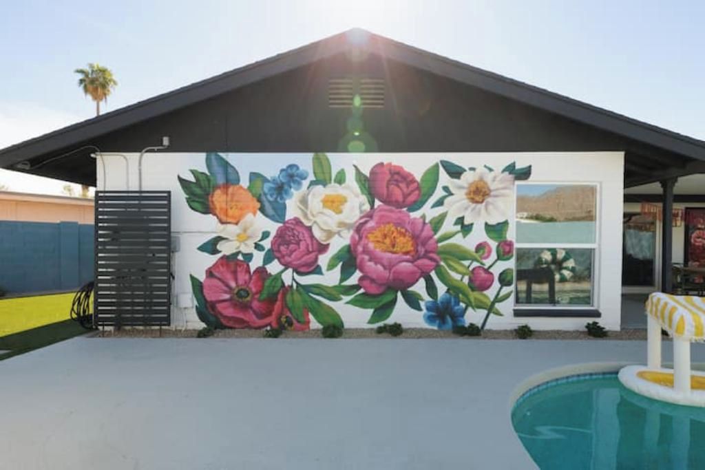 A building with a colorful floral mural on the side, a pool, and a covered patio area.