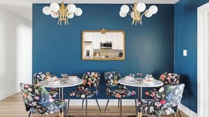 A dining area with floral-patterned chairs and a round table, a blue accent wall, and a gold-framed mirror above the table.