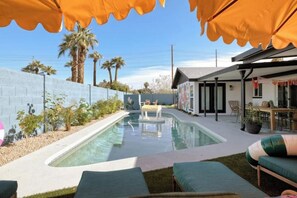 A swimming pool with lounge chairs and umbrellas, surrounded by a low wall and palm trees.