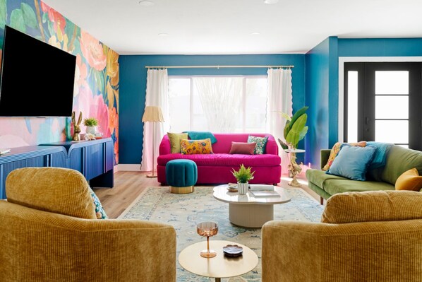 A living room with a vibrant blue wall, a pink sofa, and two armchairs.