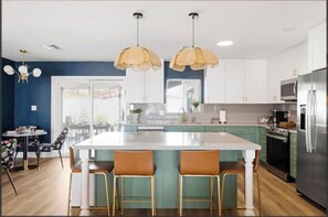 A modern kitchen with white cabinets, a central island with bar stools, and pendant lighting.