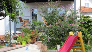 Un espacio exterior residencial con un tobogán rojo, plantas en macetas y una silla de madera.