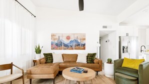 Una sala de estar con un sofá modular, una mesa de centro redonda, un sillón verde y un cuadro de un paisaje desértico.
